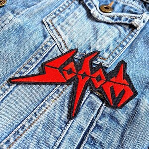 May include: Red and black embroidered patch with the word "SICK" in a stylised font. The patch is sewn onto a blue denim jacket.