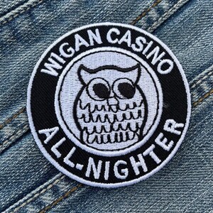 Op de afbeelding: Zwart-wit geborduurde patch met de tekst "Wigan Casino All-Nighter" en een witte uil met zwarte ogen in het midden.