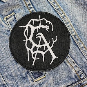 May include: Black and white embroidered patch featuring a stylised design of a tree with branches forming the letters "GA".