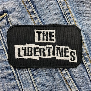 Puede incluir: Parche bordado en blanco y negro con el texto "The Libertines" sobre un fondo de mezclilla.