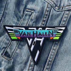 Op de afbeelding: Een geborduurde zwarte en witte patch met de tekst "Van Halen" in een kleurrijk, gestreept ontwerp. De patch heeft een gestileerde "V"-vorm.