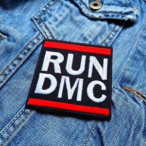 May include: A black and red embroidered patch with the text "RUN DMC" in white lettering.