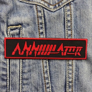 May include: A black and red embroidered patch with the word "Annihilator" in a stylized font.