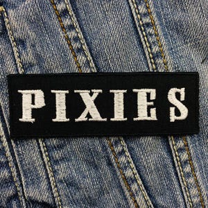 Può includere: Toppa ricamata in bianco e nero con la parola "PIXIES" in lettere bianche su sfondo nero.