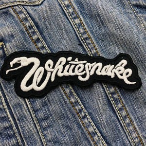 May include: Black and white embroidered patch with the text "Whitesnake" in a stylised font. The patch features a snake design.