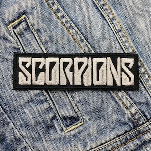Könnte beinhalten: Schwarz-weiß gestickter Patch mit dem Wort "SCORPIONS" in weißen Buchstaben auf schwarzem Hintergrund.