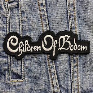 May include: Black and white embroidered patch with the text "Children Of Bodom" on a denim background.