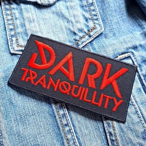 Puede incluir: Un parche negro con las palabras "DARK TRANQUILLITY" en letras bordadas rojas.