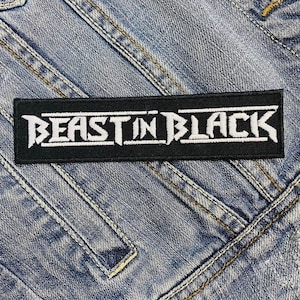 Może przedstawiać: Czarno-biały haftowany naszywka z tekstem "Beast in Black" na dżinsowym tle.