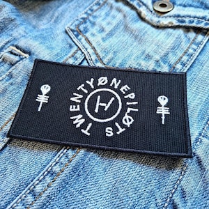 Op de afbeelding: Zwart-witte geborduurde patch met de tekst "Twenty One Pilots" en een gestileerde "H" in een cirkel. De patch heeft ook twee kleine skelet handsymbolen.