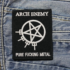 May include: Black embroidered patch with the text "ARCH ENEMY" above a white pentagram symbol inside a circle. Below the symbol, the text reads "PURE FUCKING METAL". The patch is sewn onto a denim fabric.
