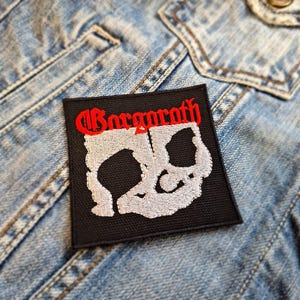 May include: Black and white embroidered patch with the band name "Gorgoroth" in red lettering. The patch features a skull design.