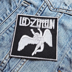 May include: Black and white embroidered patch with the text "Led Zeppelin" and a white angel with wings on a denim jacket.