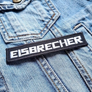 May include: A close-up of a blue denim jacket with a black patch that says "EISBRECHER" in white letters.