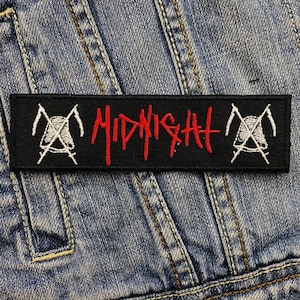 Op de afbeelding: Zwart rechthoekig embleem met het woord "MIDNIGHT" in rood en witte zeis- en doodshoofdmotieven. De patch is geplaatst op een blauwe denim stof achtergrond.