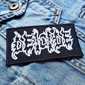 May include: Black embroidered patch with white lettering that reads "DECAPITATED".