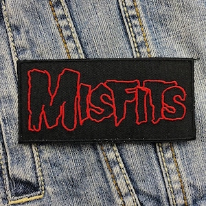 Puede incluir: Un parche bordado negro con la palabra "Misfits" en letras rojas. El parche está sobre un fondo de mezclilla.
