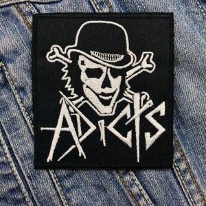 May include: Black and white embroidered patch featuring a skull wearing a bowler hat and the word "ADICTS" in white lettering.