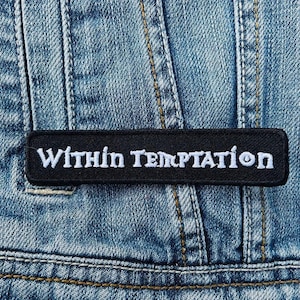 May include: Black and white embroidered patch with the text "Within Temptation" on a denim background.