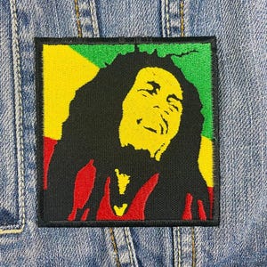 Könnte beinhalten: Gestickter Aufnäher mit einem Porträt von Bob Marley vor einem gelben, grünen und roten Hintergrund. Der Aufnäher ist aus Stoff und hat einen schwarzen Umriss.