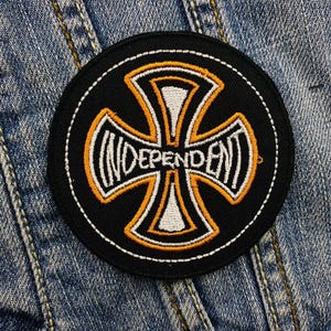 May include: A black and white embroidered patch with an orange cross and the word "Independent" written in a stylized font.