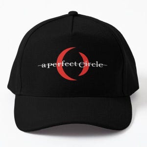 Puede incluir: Gorra de béisbol negra con la inscripción "a perfect Circle" en blanco y un diseño circular rojo. La gorra tiene una visera curva y un botón en la parte superior. Un accesorio de moda.