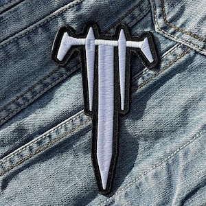 Könnte beinhalten: Weißer gestickter Aufnäher mit einem dreiköpfigen Schwert auf einem blauen Jeansstoff.