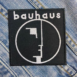Puede incluir: Parche bordado en blanco y negro con la palabra "bauhaus" y un diseño de rostro estilizado.