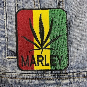 Könnte beinhalten: Ein gestickter Patch mit einem Marihuana-Blatt in Rot, Gelb und Grün mit dem Wort "MARLEY" in Schwarz.