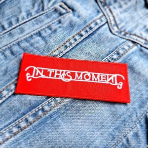 Könnte beinhalten: Roter gestickter Aufnäher mit weißer Aufschrift "In This Moment".