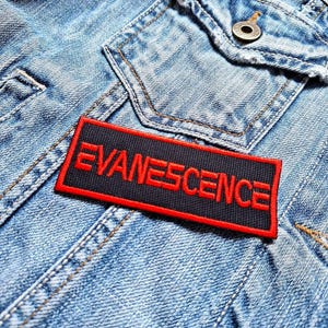 May include: A black and red patch with the word "EVANESCENCE" in red lettering on a denim jacket.