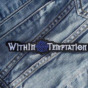 May include: A black and white embroidered patch with the text "Within Temptation" and a blue and white symbol in the center. The patch is sewn onto a blue denim fabric.