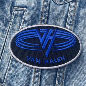 May include: A black and blue embroidered patch with the text "Van Halen" and a stylised "VH" logo.