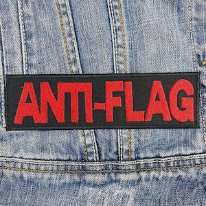 May include: A black patch with the words "ANTI-FLAG" in red lettering sewn onto a blue denim jacket.