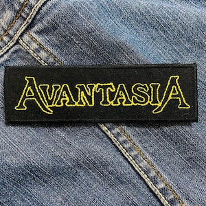 Może przedstawiać: Czarna naszywka z tkaniny z haftowanym napisem "AVANTASIA" w kolorze żółtym.
