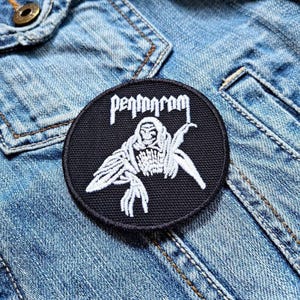 May include: Black and white embroidered patch with a hooded figure and the text "Pentagram" on a denim jacket.