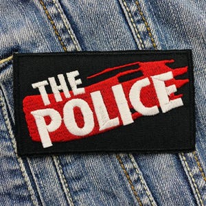 Peut inclure: Patch brodé noir et rouge avec le texte "THE POLICE" en lettres blanches.