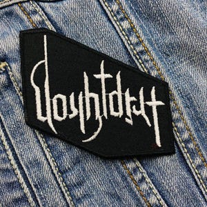 Op de afbeelding: Zwart geborduurd embleem met het woord "Youthdry" in witte gotische letters. Het embleem heeft een vijfhoekige vorm en staat op een denim achtergrond.