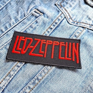 May include: A black rectangular patch with the red embroidered text "LED ZEPPELIN" is attached to a light blue denim jacket. The patch is centered, and the text is in a bold, stylized font.