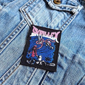 May include: Black and white embroidered patch with the word "GRILLLEY" in pink letters. The patch features a blue background with a pink and white design.