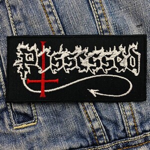 May include: Black embroidered patch with a white inverted cross and the word "Sacrilege" in white lettering.