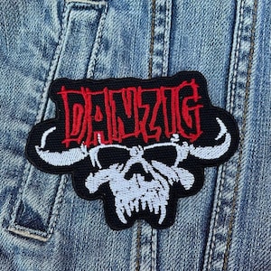 Może przedstawiać: Naszywka haftowana w kolorze czarnym i białym z napisem "DANZIG" w czerwonych literach nad czaszką z rogami.