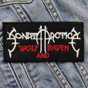 Puede incluir: Parche negro con texto bordado en blanco "SONATA ARCTICA" y texto en rojo "WOLF RAVEN AND" sobre un fondo de mezclilla.
