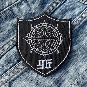 May include: Black embroidered patch with a white design of a circle with a cross inside and the number 96 below it. The patch is shaped like a shield.