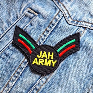 Peut inclure: Patch brodé noir et vert avec un cercle jaune qui dit "JAH ARMY" sur un fond en jean bleu.