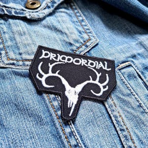 May include: Black and white embroidered patch with a deer skull and antlers. The text "DRICORDIAL" is written in white on a black background.