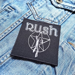 Könnte beinhalten: Schwarzer gestickter Patch mit dem Wort "Rush" in weißen Buchstaben und einer stilisierten weißen Figur in einem Kreis.