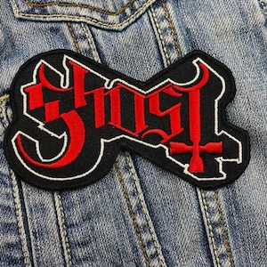 Puede incluir: Un parche bordado negro y rojo con la palabra "Ghost" en una fuente estilizada. El parche presenta una cruz invertida roja.