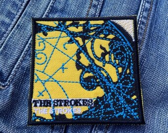 May include: Yellow and blue embroidered patch with the text "The Strokes" and a graphic design of a map.