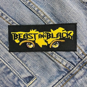 Puede incluir: Parche bordado negro y amarillo con el texto "Beast in Black" y dos ojos estilizados.